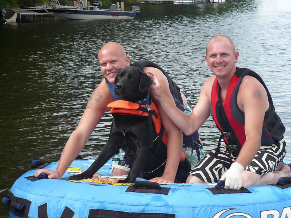 Two men and black dog on inner tube.