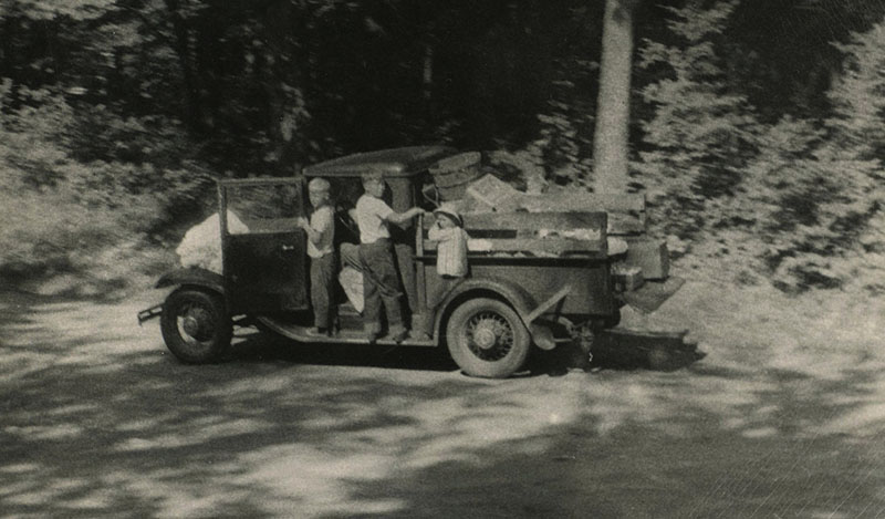 Historic photo of kids on an old car hauling garbage.