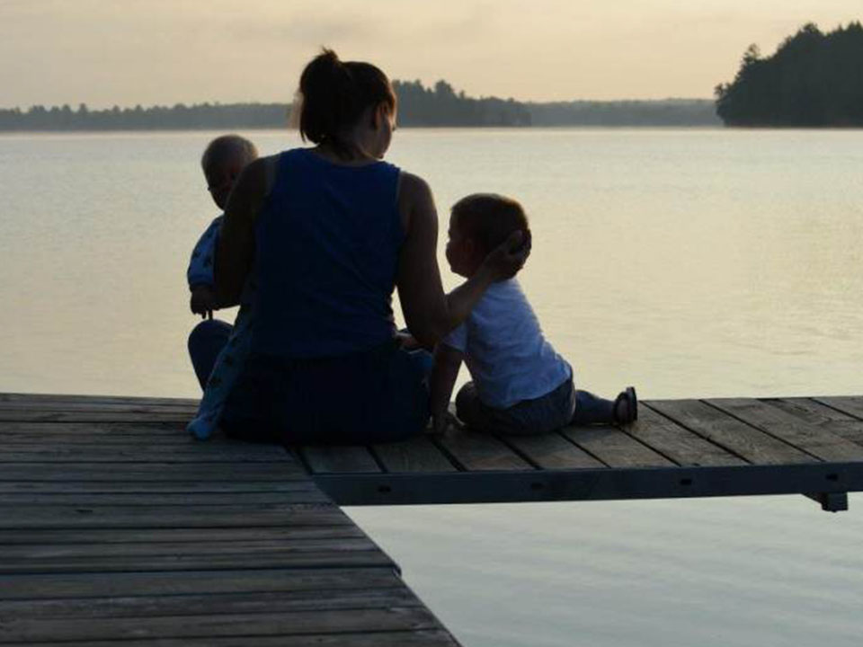 Mother with children sitting on the dock at sunset