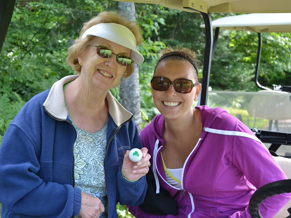 Two women posing with golf ball on golf cart.