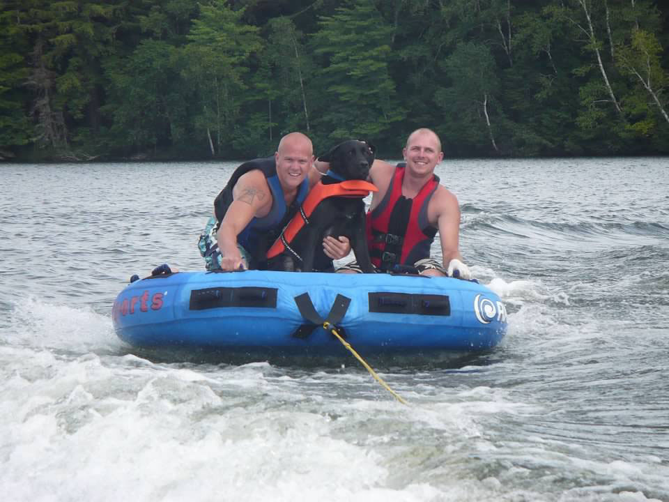 Two men and black dog on inner tube.