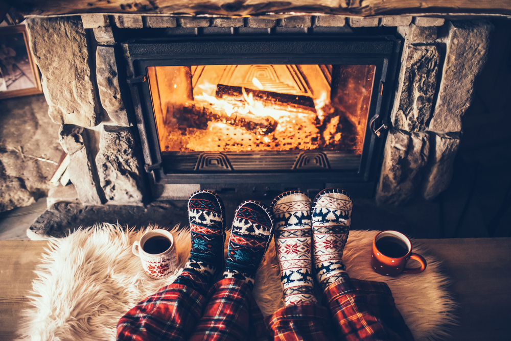 A pair of feet are adorned in cozy socks, next to two mugs and in front of a fireplace.