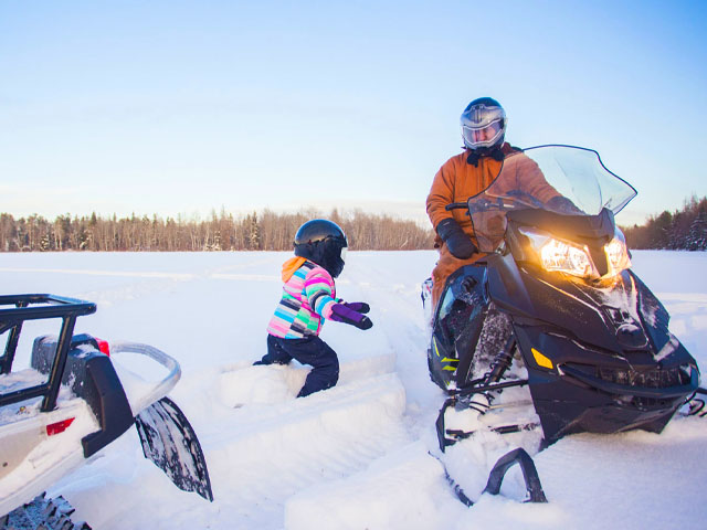 Child getting on a snowmobile with adult